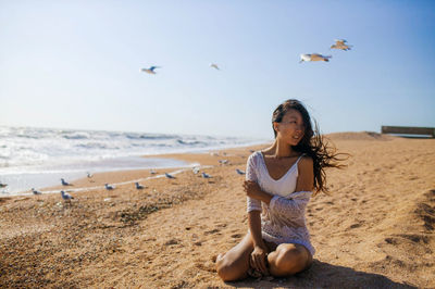 Portrait of woman sitting on beach against sky