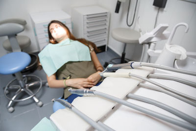 Close-up of dental equipment against female patient sitting in clinic