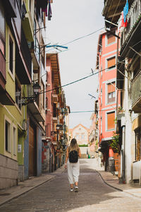 Rear view of woman walking on footpath amidst buildings in city