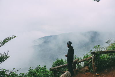 Man standing by plants and railing against sky