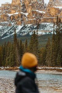 Blurred anonymous traveler admiring snowy castle mountain and coniferous trees while standing on river coast in banff national park