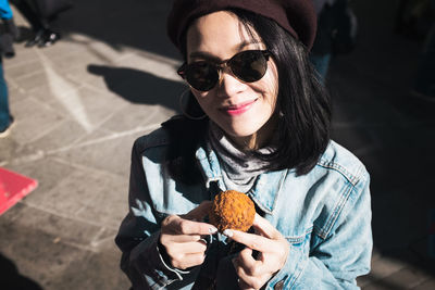 Portrait of smiling woman wearing sunglasses holding sweet food in city