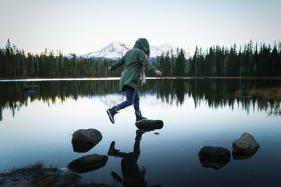 Man standing on rock by lake against sky