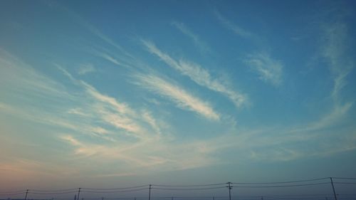 Low angle view of power lines against cloudy sky