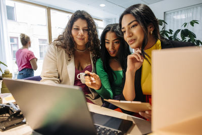 Businesswoman sharing laptop with female entrepreneurs at office