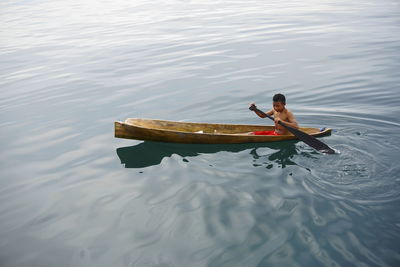 Shirtless boy oaring boat in sea