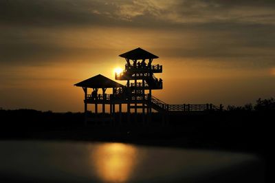 Silhouette built structure by sea against orange sky