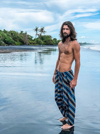 Shirtless man standing at beach against sky