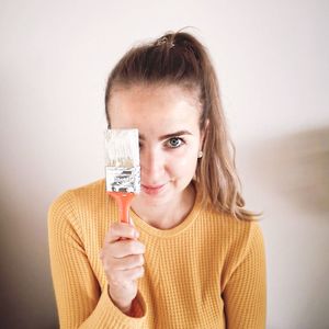 Close-up portrait of smiling young woman holding a paint brush over white background