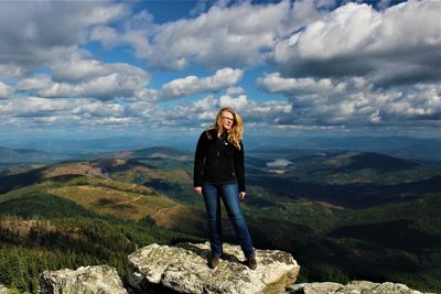 Young woman standing on cliff against cloudy sky