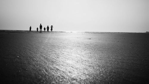 People walking at beach against clear sky