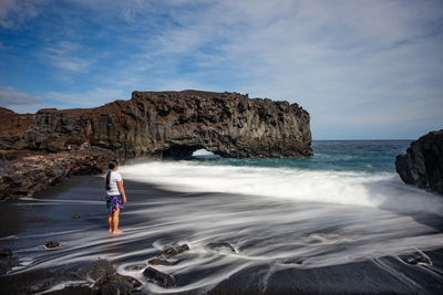 Man standing on rock by sea against sky