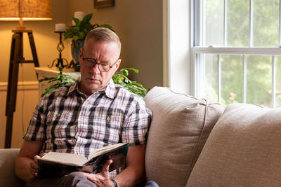 Senior man reading man sitting on sofa at home