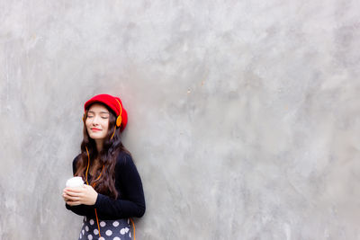 Portrait of beautiful young woman standing against wall during winter