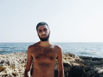 Young man standing at beach against clear sky