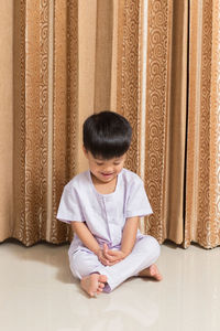 Boy sitting against curtain at home