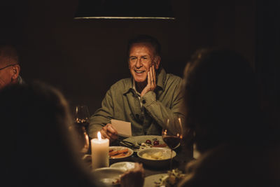 Smiling senior man enjoying candlelight dinner party at illuminated table