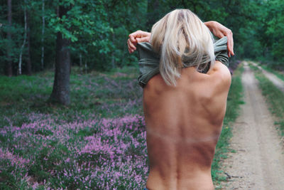 Rear view of woman removing clothes while standing in forest