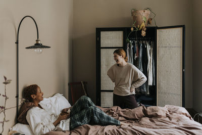 Non-binary couple laughing with each other in bedroom at home