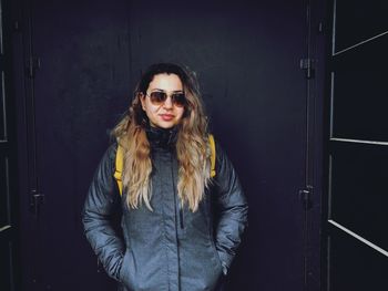 Portrait of smiling young woman standing against wall