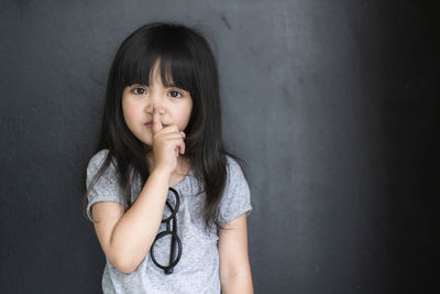 Portrait of girl with finger on lips standing against gray wall