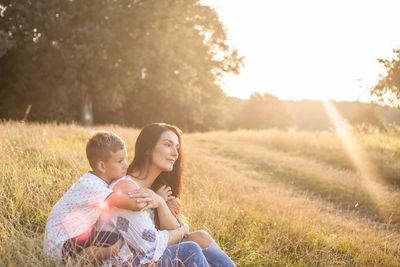 Mother and son relaxing on field in sunny day