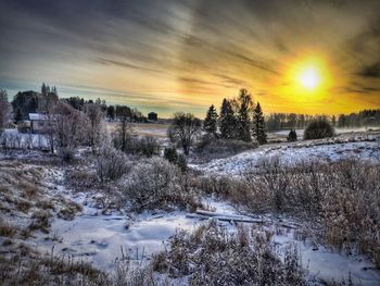 Snow covered landscape against sky during sunset