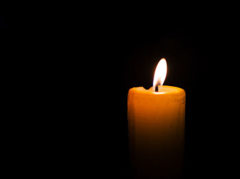 Close-up of burning candle against black background