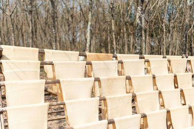 Stack of empty chairs in row against trees