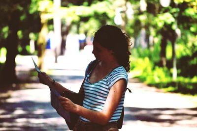 Woman holding mobile phone while standing on tree