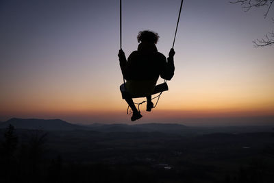 Silhouette man sitting against sky during sunset