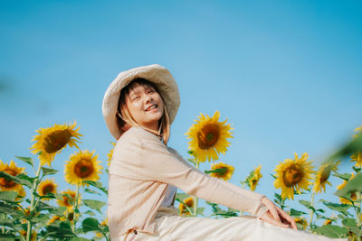 Portrait of smiling young woman with sunflower against sky