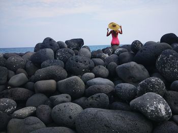 Rear view of woman wearing sitting on rocks at beach in san giovanni li cuti