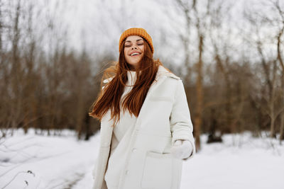 Smiling young woman standing on snow covered land during winter