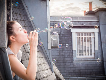 Side view of woman blowing bubbles from window