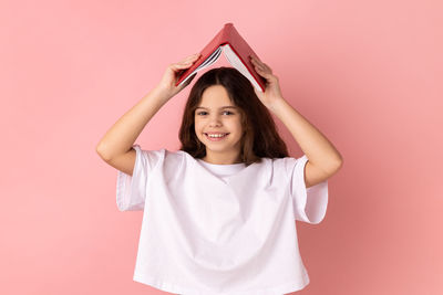 Portrait of young woman holding gift against pink background