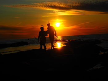 Silhouette men standing at beach during sunset