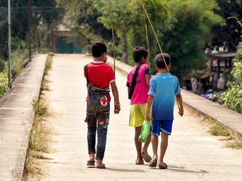 Rear view of friends walking on road along trees