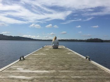 Woman sitting on pier over lake against sky