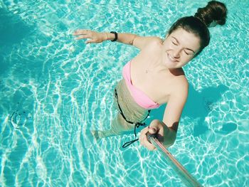 High angle view of woman wearing bikini taking selfie from monopod in swimming pool on sunny day