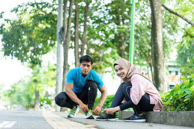 Young couple sitting on plant against trees