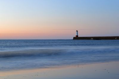 Lighthouse by sea against sky during sunset