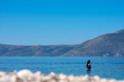 Woman in sea against clear blue sky
