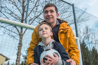 Father and son playing soccer ball on playground, dad teaches son to play on football field activity