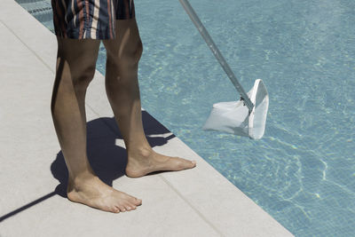 Close-up view of an unrecognizable man cleaning the surface of his home pool with a cleaning net