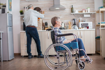 Disabled woman sitting on wheelchair with man in background at home