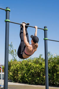 Low angle view of girl hanging on pole against clear blue sky