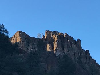 Low angle view of rocky mountains against clear blue sky