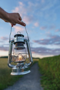 Close-up of woman holding lantern against sky during sunset