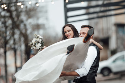 Groom lifting bride while standing outdoors
